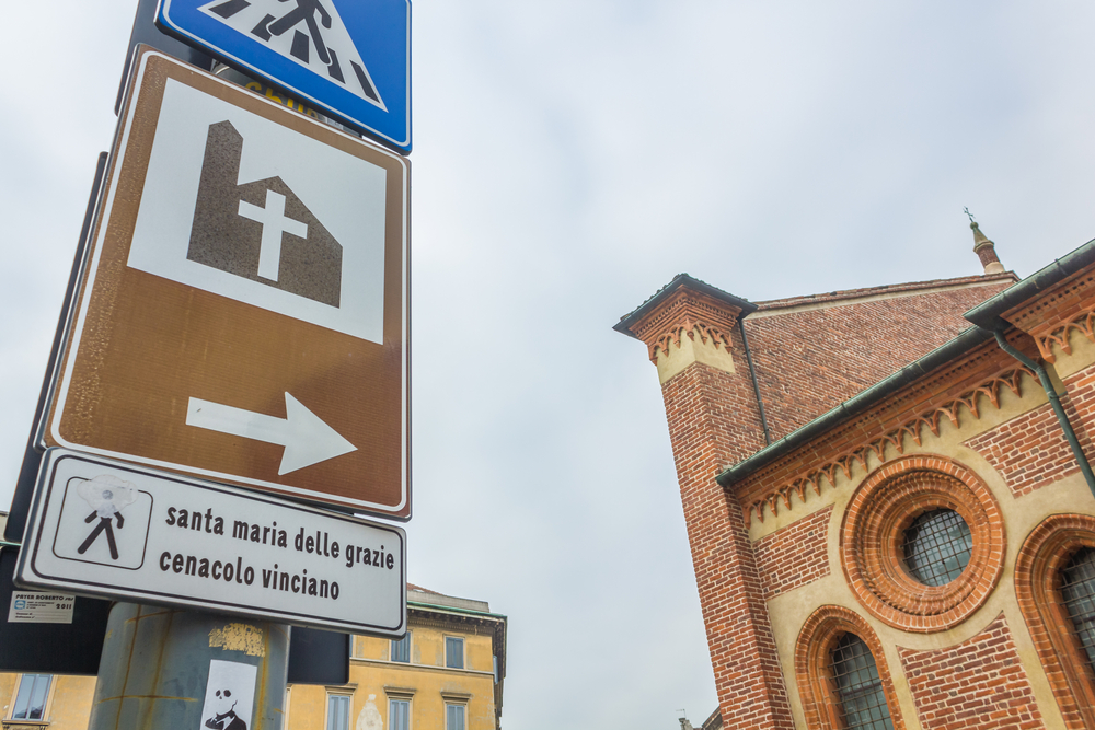 close up on road sign to Milan's Santa Maria Delle Grazie, hosting The Last Supper mural painting by Leonardo da Vinci.