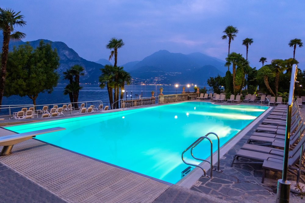 Empty hotel pool at night. Lake Como, palms and mountains on background. 