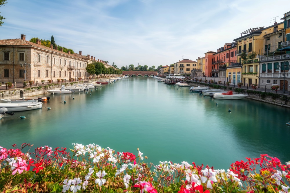 Peschiera del Garda Lake Garda Veneto Italy - buildings on both sides with a wide canal of water in the middle. Flowers in the foreground