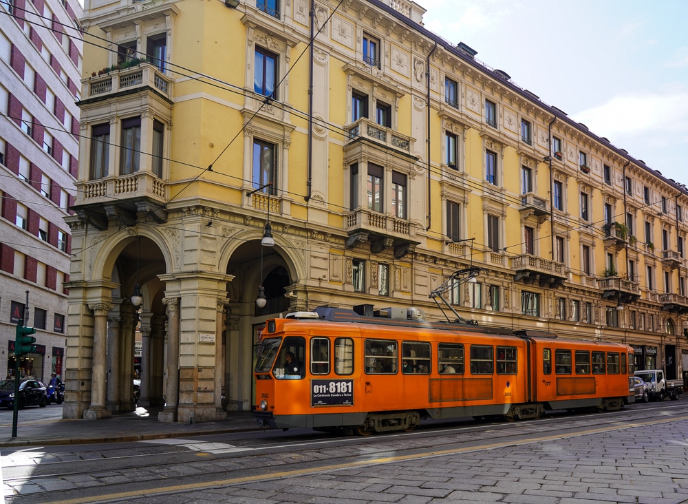 a yellow historic building in Turin Italy with an orange streetcar tram passing by