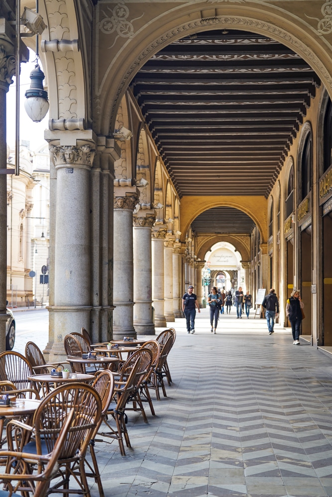 Turin Italy porticoes (covered sidewalks) with tables and chairs from a cafe in the foreground