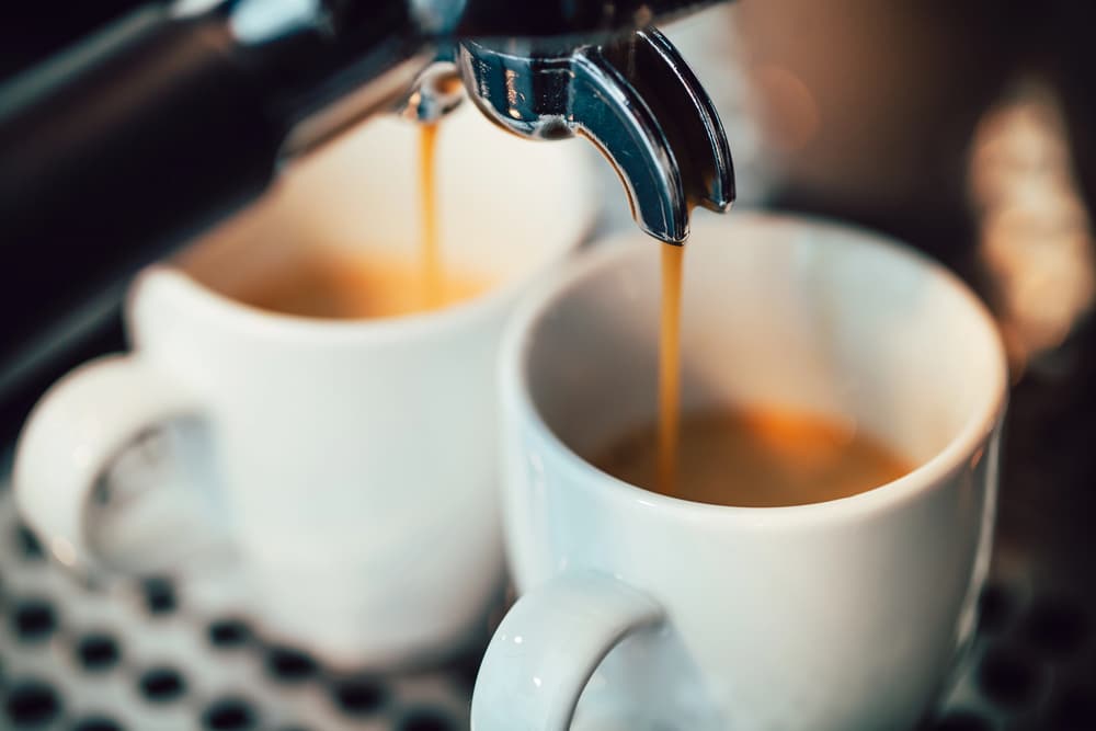 close up of 2 espresso cups getting filled by an espresso machine