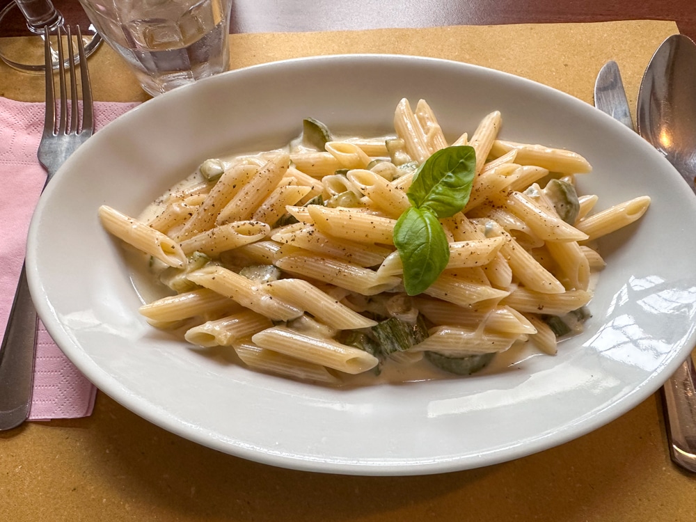 Plate of penne on a table at a restaurant with a sprig of basil