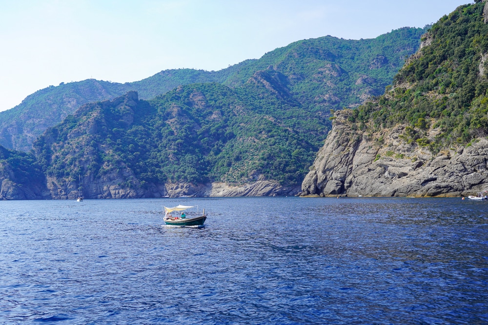 boat on the sea with green rocky cliffs behind in Liguria