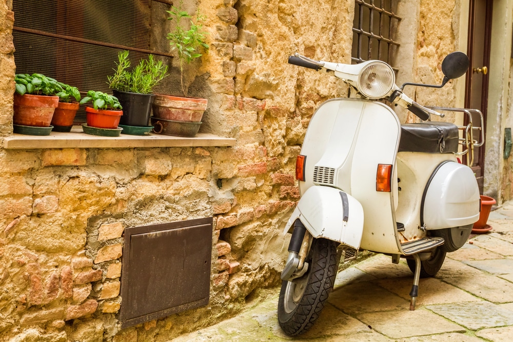 Italy Street Scene with a vespa and stone building behind it with plants on the window ledge