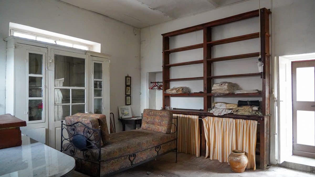 A room in an old house with high ceilings and a tall wooden shelf with some other furniture scattered around the room