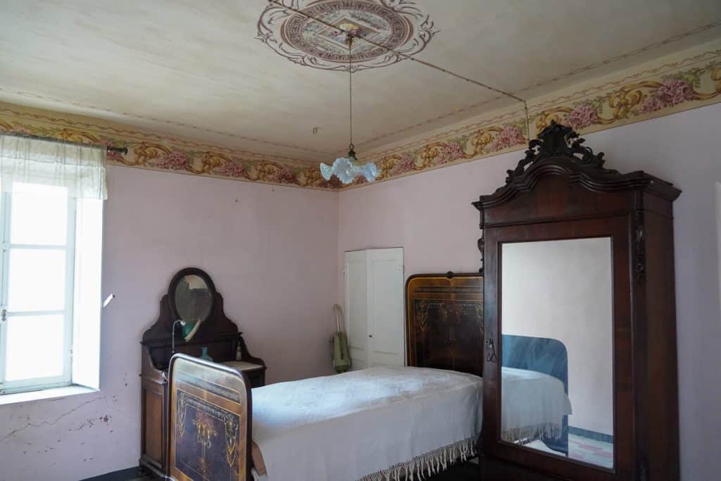 room in an old Italian house with a painted ceiling and an antique bed, vanity, and wardrobe.