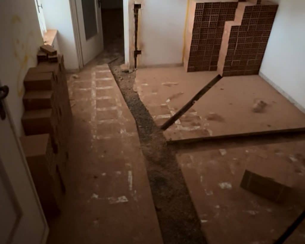 room with red tiles and stacks of bricks, channels are dug out in the floors for future pipes and electrical