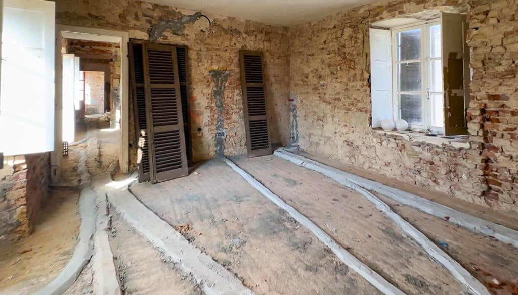 a brick room under renovation with plumbing and electrical lines running along the floor covered in concrete