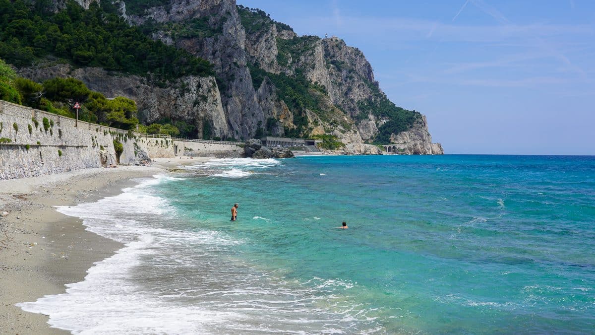 turquoise water at the Baia dei Saraceni along a dramatic rocky coastline with 2 men in the water near Noli Italy